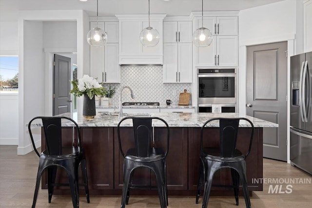 2895 Evening Sun Dr, Twin Falls, ID 83301 - kitchen featuring appliances with stainless steel finishes, decorative backsplash, white cabinetry, and an island with sink