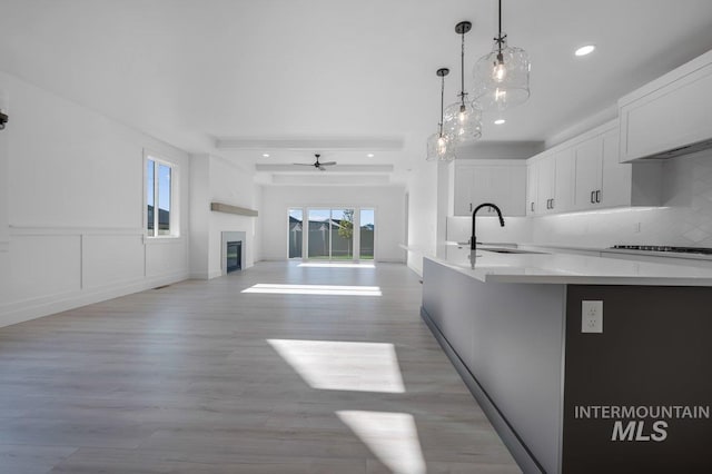 kitchen featuring light hardwood / wood-style floors, white cabinets, decorative light fixtures, backsplash, and sink