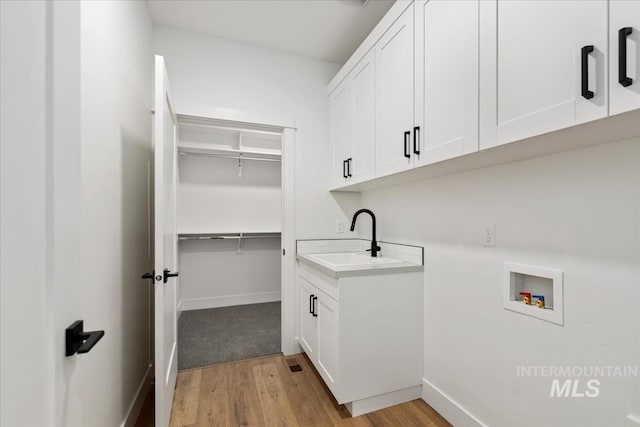 clothes washing area with light wood finished floors, a sink, hookup for a washing machine, baseboards, and cabinet space
