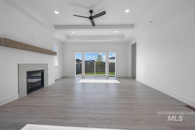 unfurnished living room with a tray ceiling, a tiled fireplace, light wood-type flooring, and ceiling fan