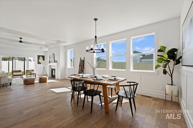 dining space with wood finished floors, visible vents, baseboards, a glass covered fireplace, and ceiling fan with notable chandelier