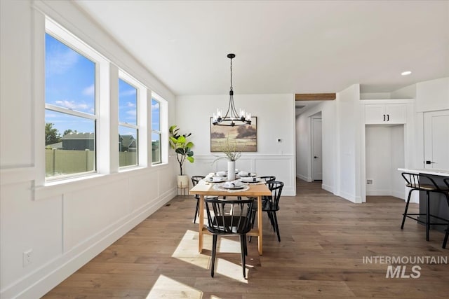 dining space with light wood-style floors, a decorative wall, baseboards, and a notable chandelier