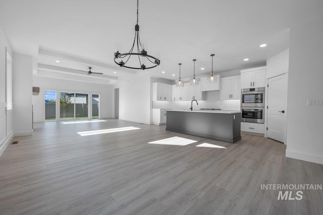 kitchen featuring light wood-type flooring, double oven, a center island with sink, and pendant lighting