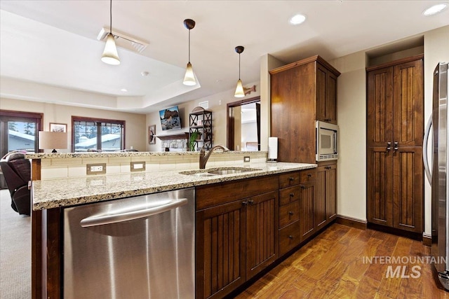 kitchen featuring kitchen peninsula, appliances with stainless steel finishes, light stone countertops, sink, and pendant lighting