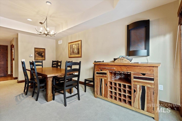 dining space featuring a tray ceiling, light colored carpet, and a notable chandelier