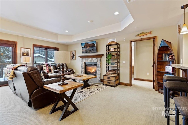 carpeted living room with a raised ceiling, a stone fireplace, and plenty of natural light