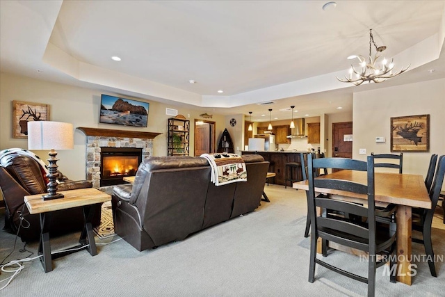 living room featuring a fireplace, a tray ceiling, a chandelier, and light colored carpet