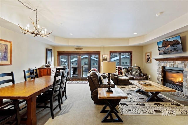 carpeted living room featuring a stone fireplace and a chandelier