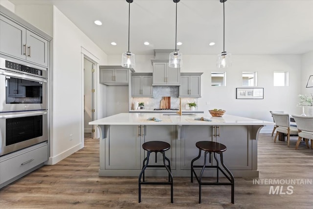 8820 E Snow Drop St, Nampa, ID 83687 - kitchen with a kitchen bar, wood finished floors, gray cabinetry, light countertops, and double oven