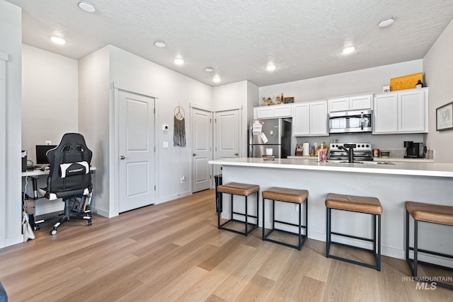 2312 E Spice Loop Unit 2, Nampa, ID 83687 - kitchen with appliances with stainless steel finishes, a kitchen breakfast bar, light wood-type flooring, white cabinets, and light countertops