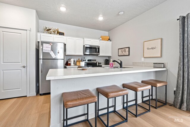 2312 E Spice Loop Unit 2, Nampa, ID 83687 - kitchen featuring stainless steel appliances, a kitchen bar, light wood-type flooring, white cabinetry, and a textured ceiling