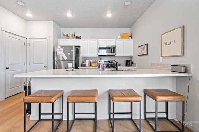 2312 E Spice Loop Unit 2, Nampa, ID 83687 - kitchen featuring appliances with stainless steel finishes, a kitchen breakfast bar, white cabinetry, light wood-type flooring, and a textured ceiling