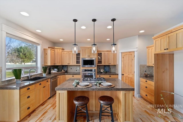 kitchen featuring light wood finished floors, light brown cabinetry, appliances with stainless steel finishes, and a sink