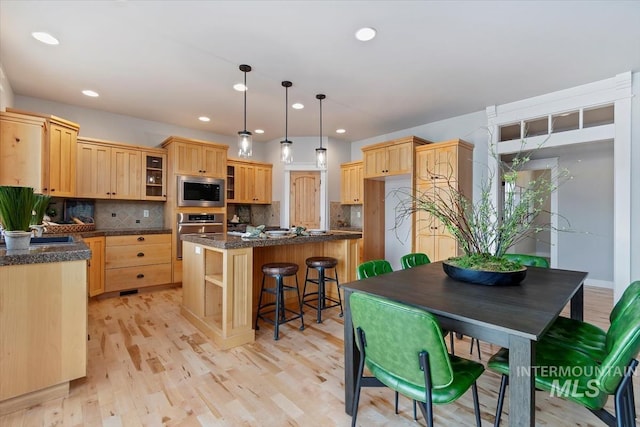 kitchen featuring light brown cabinetry, appliances with stainless steel finishes, glass insert cabinets, a kitchen island, and light wood-type flooring