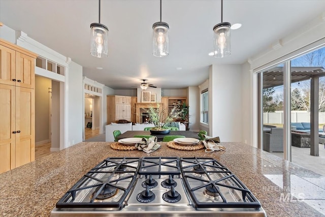 kitchen featuring a ceiling fan, open floor plan, a lit fireplace, light brown cabinetry, and stainless steel gas stovetop