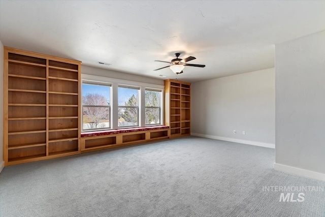 carpeted spare room with ceiling fan, built in shelves, visible vents, and baseboards