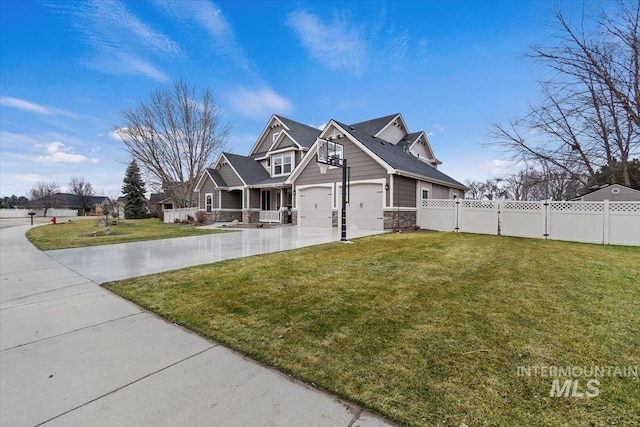 view of side of property featuring stone siding, concrete driveway, fence, and a lawn