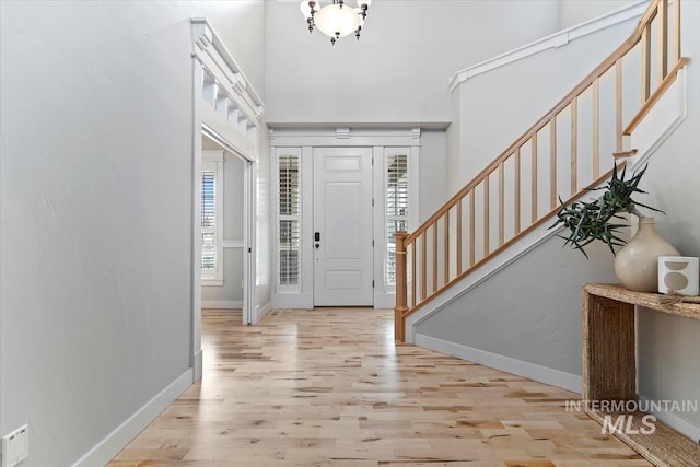 foyer with a towering ceiling, light wood finished floors, baseboards, and stairway