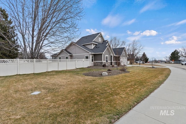 view of home's exterior with stone siding, roof with shingles, fence, and a lawn