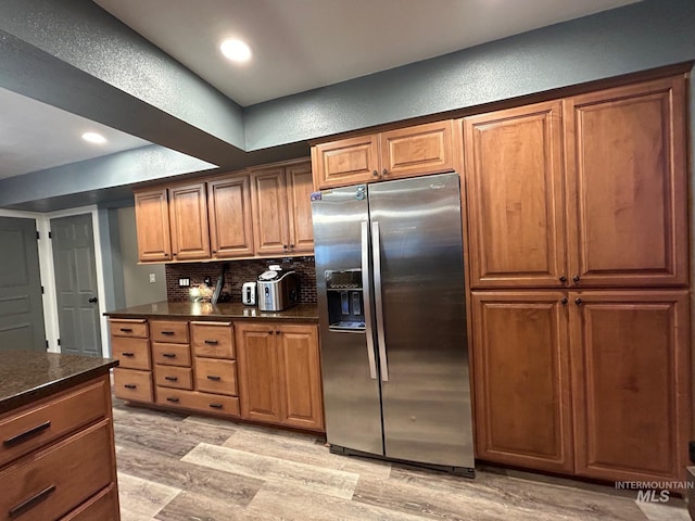 kitchen with stainless steel fridge with ice dispenser, light hardwood / wood-style flooring, and backsplash