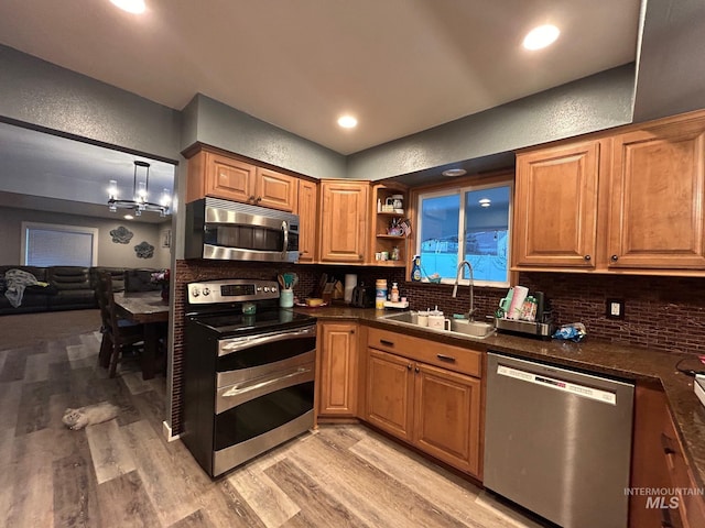 kitchen with decorative backsplash, light hardwood / wood-style flooring, stainless steel appliances, sink, and decorative light fixtures