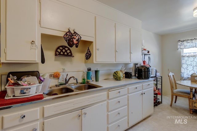 kitchen featuring sink, light tile patterned floors, and white cabinets