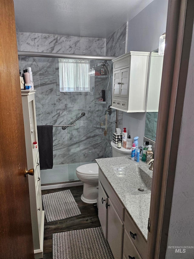 bathroom featuring wood-type flooring, a shower with shower door, toilet, and vanity