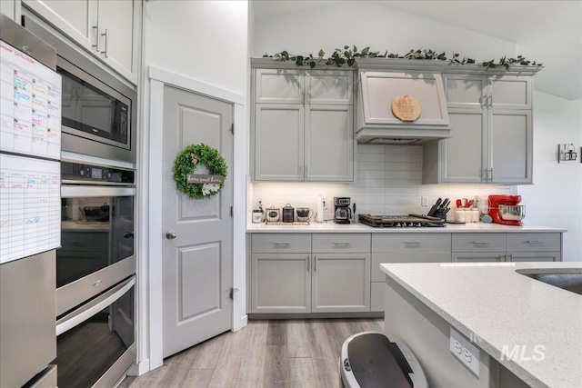209 W 13th Ave, Jerome, ID 83338 - kitchen featuring gray cabinets, light wood-type flooring, stainless steel appliances, backsplash, and custom exhaust hood