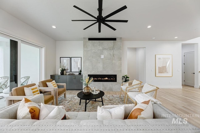 living room with light hardwood / wood-style flooring, a tiled fireplace, and ceiling fan