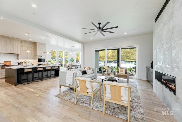 living room with a tile fireplace, light hardwood / wood-style floors, and ceiling fan