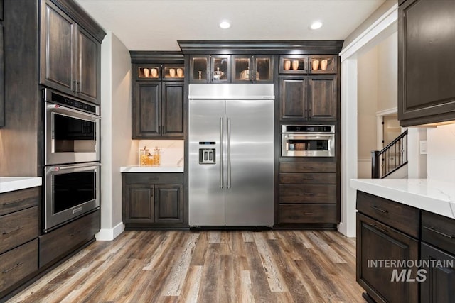 kitchen with appliances with stainless steel finishes, glass insert cabinets, and dark brown cabinets