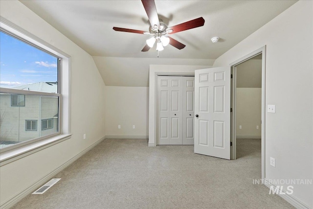 unfurnished bedroom featuring vaulted ceiling, light colored carpet, a closet, and ceiling fan