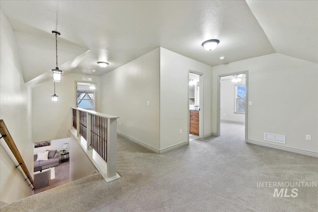 bonus room with lofted ceiling, light colored carpet, and a textured ceiling