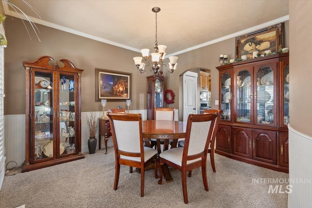 dining room with a wainscoted wall, arched walkways, light carpet, crown molding, and a chandelier