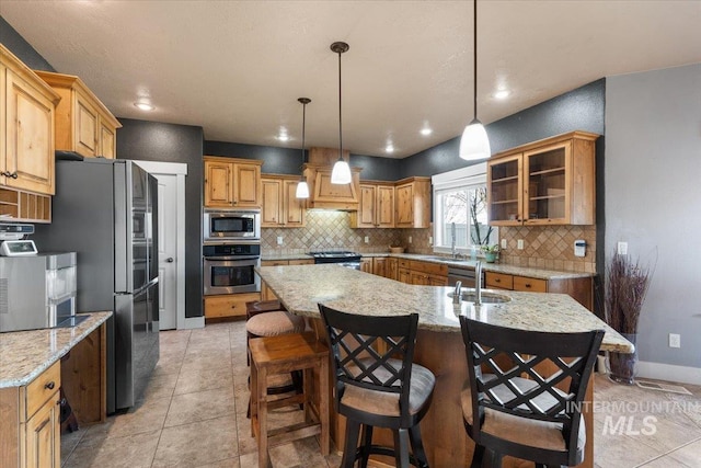 kitchen with backsplash, baseboards, a center island with sink, and appliances with stainless steel finishes