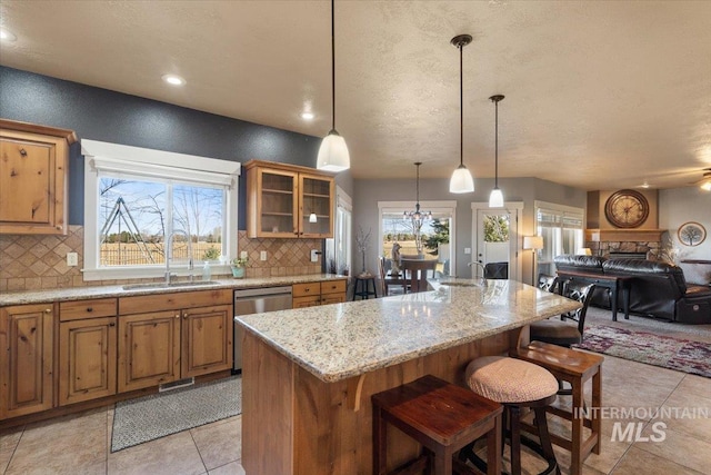 kitchen featuring tasteful backsplash, open floor plan, light stone counters, brown cabinetry, and a sink