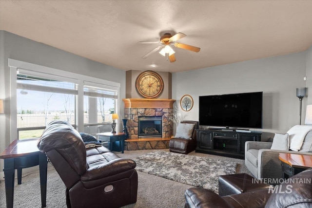 living area featuring carpet, a stone fireplace, and a ceiling fan