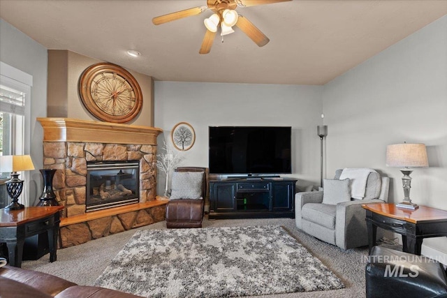 living room with carpet flooring, a stone fireplace, and a ceiling fan