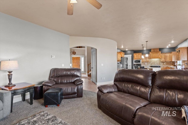 living room with light tile patterned floors, a ceiling fan, baseboards, arched walkways, and light carpet