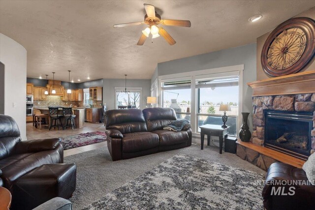 living room with light tile patterned floors, a fireplace, ceiling fan, a textured ceiling, and light colored carpet