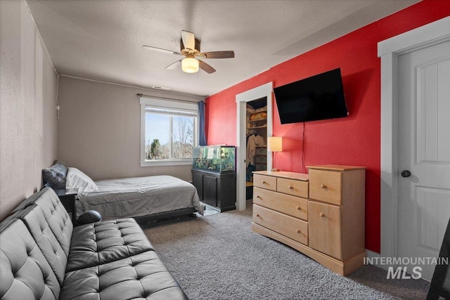 bedroom with a spacious closet, a textured wall, carpet floors, and ceiling fan