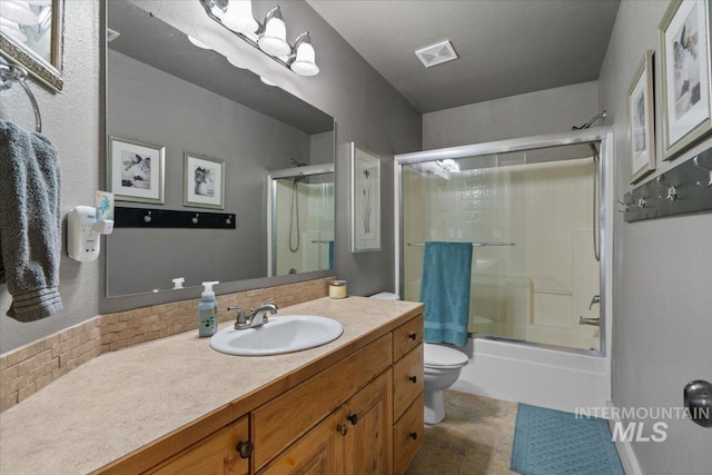 bathroom featuring visible vents, toilet, vanity, and bath / shower combo with glass door