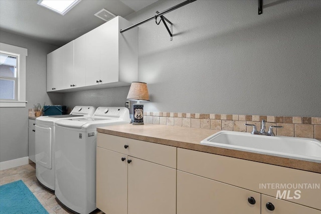 laundry area featuring washing machine and clothes dryer, visible vents, baseboards, cabinet space, and a sink