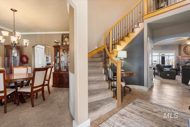 stairway with arched walkways, a notable chandelier, tile patterned flooring, and crown molding