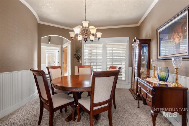 dining space with an inviting chandelier, light colored carpet, and a wainscoted wall