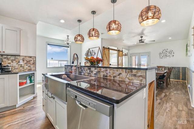 kitchen featuring a center island with sink, stainless steel dishwasher, backsplash, and pendant lighting