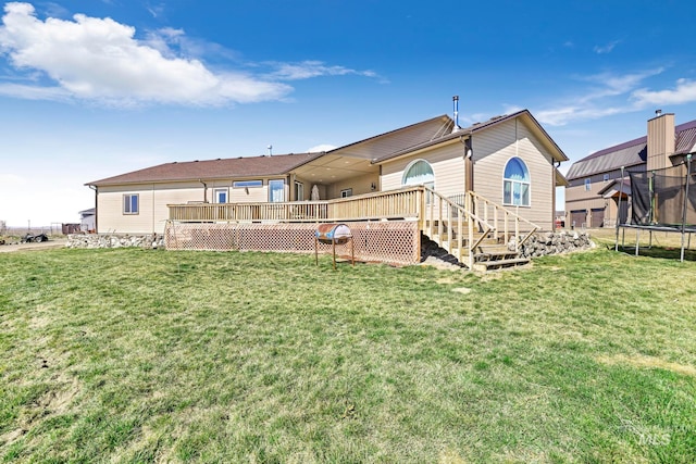 rear view of house with a lawn, a trampoline, and a wooden deck