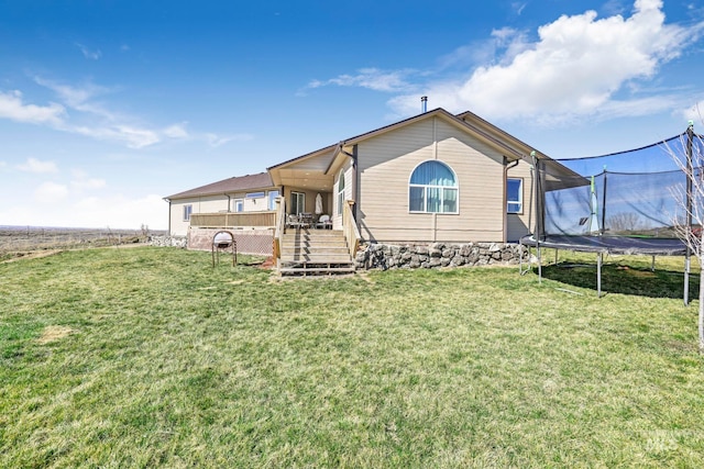 back of house featuring a deck, a trampoline, and a lawn