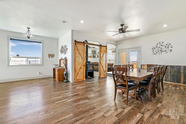 dining room with dark hardwood / wood-style floors, ceiling fan with notable chandelier, french doors, and a barn door