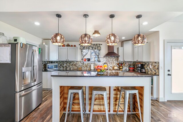 kitchen with stainless steel appliances, dark wood-type flooring, wall chimney exhaust hood, tasteful backsplash, and decorative light fixtures